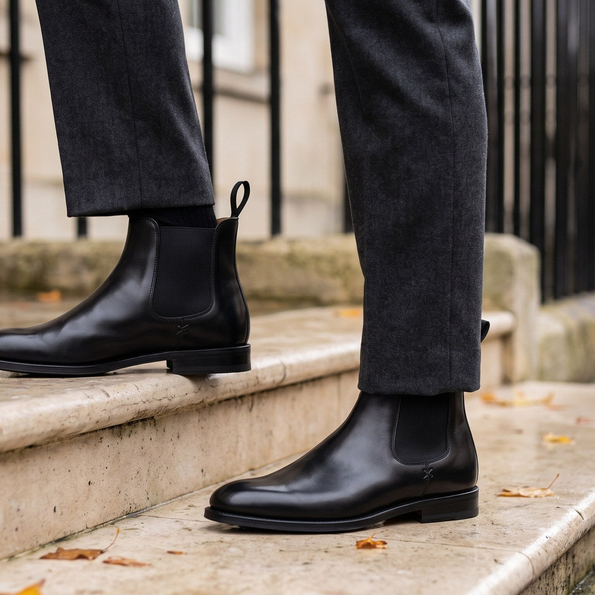Brecon Chelsea Boot in black calf, worn with charcoal trousers on a stone step